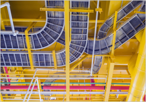 Gray tables running through cable trays installed on a yellow ceiling.